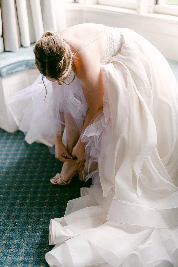 La mariée vêtue de sa belle robe de princesse enfile ses chaussures de mariage.