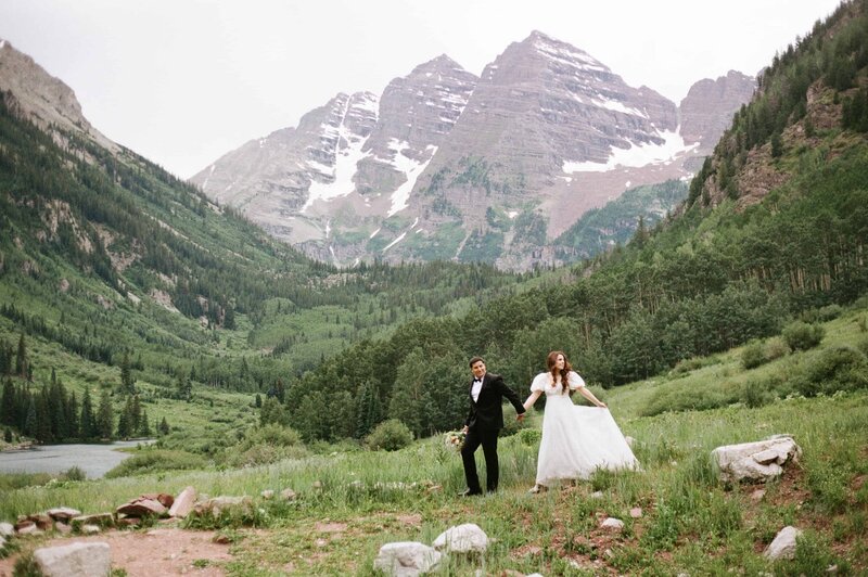 Bride and groom holding hands while walking in a meadow at the Maroon Bells Amphitheater film photography with Colorado elopement photographer and videographer packages Alpine Vows.