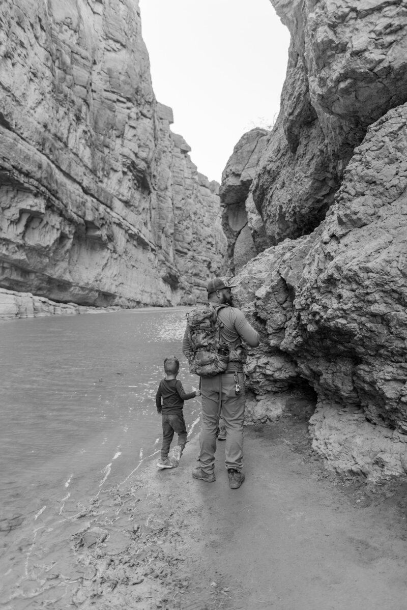 Editorial-style black and white photo of father and son hiking a riverside trail through Big Bend’s dramatic canyons, captured by luxury Texas wedding photographer Erin Marcin.