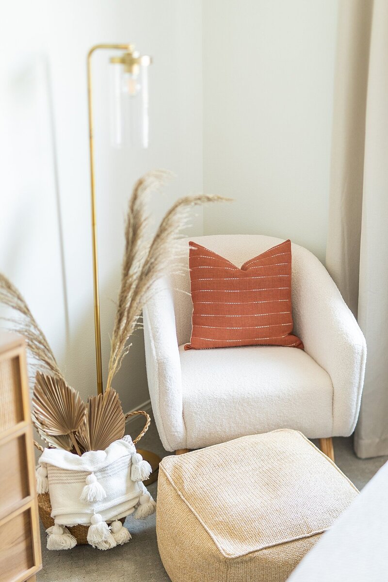 Bedroom study corner with fluffy cream chair, rust pillow, gold lamp, and foot cushion in Encinitas, California.
