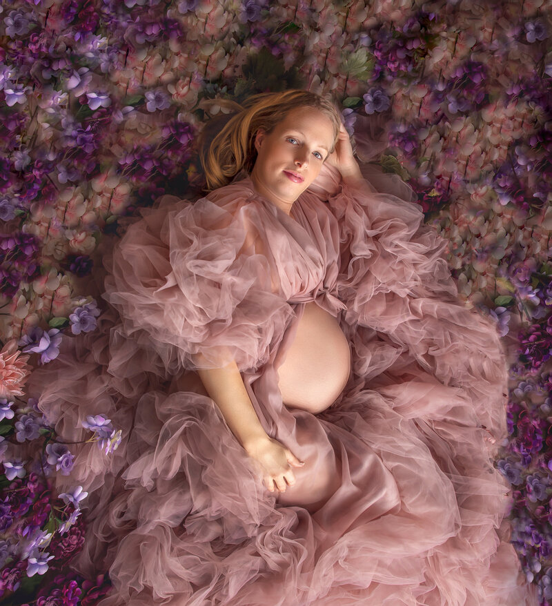 Mom in a stunning maternity gown lying on the floor, gazing at the camera in a soft, elegant pose, captured in an intimate maternity session in Ottawa."