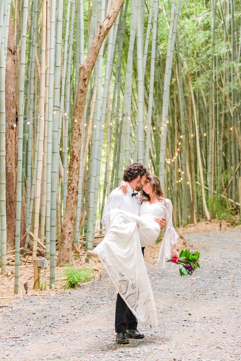 The groom carries his bride through the bamboo at Camelot Meadows.