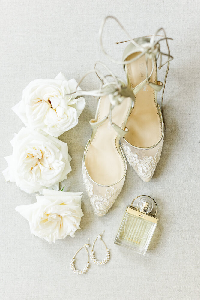 flat lay of white roses, bridal shoes, earrings, and perfume