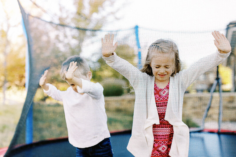 brother and sister stand on a trampoline in their backyard