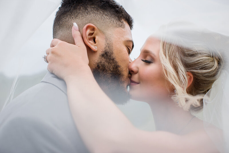 Bride and groom sharing a tender kiss under their veil, creating a dreamy and timeless wedding photo.