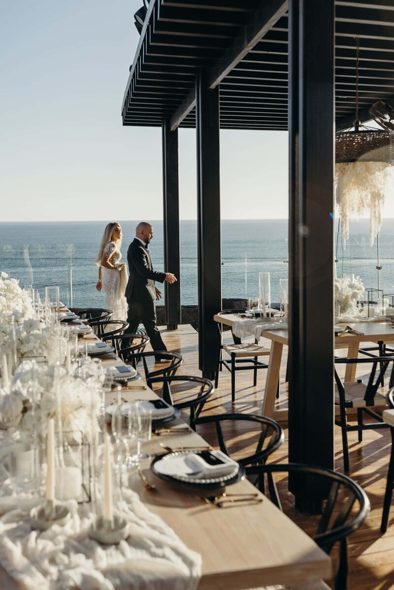 Wedding couples walks along the rooftop with the ocean behind them