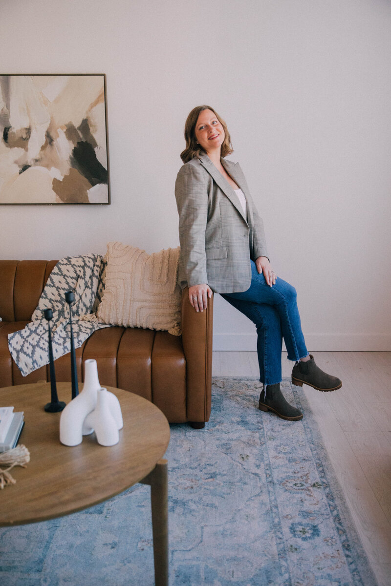 Katie, owner of Modern Mollusk, professional home stager in Snohomish County, smiling beside a styled fireplace with modern décor.