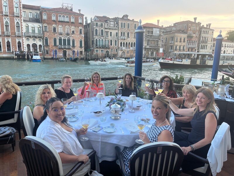 Group of women seated at round table having dinner at Gritti Palace's canalside restaurant on summer evening. 