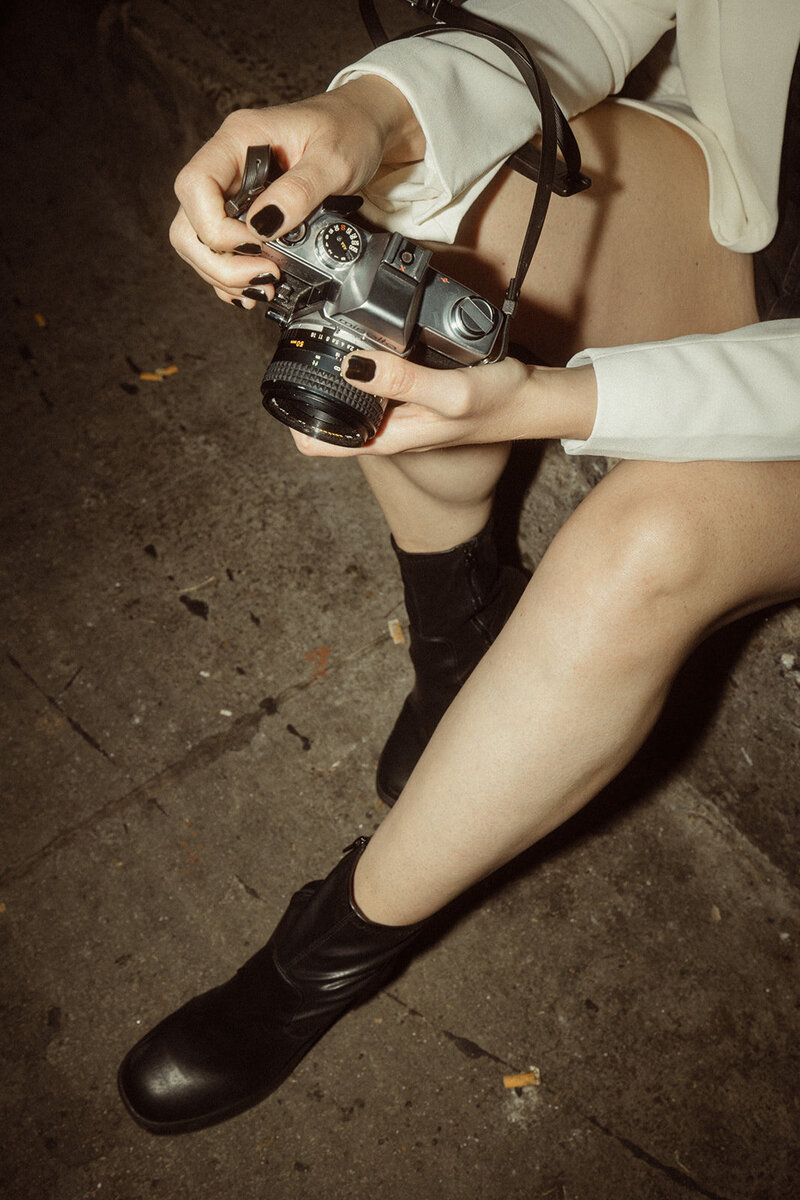 hands holding film camera with black boots in backgrounf