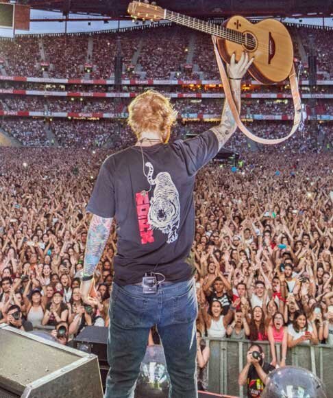 Ed Sheeran lifts guitar over his head facing thousands of cheering fans in sold-out stadium concert