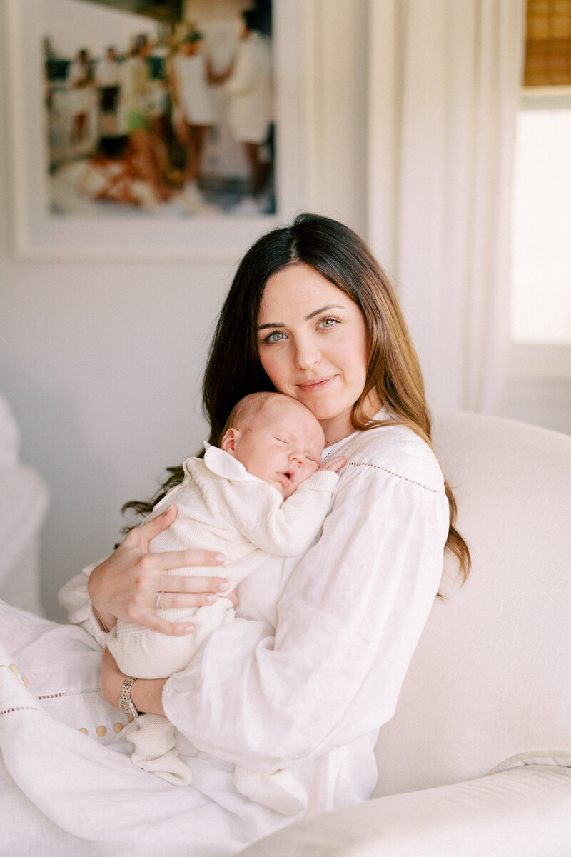 Portrait of a mom in a white dress holding her newborn baby on her chest