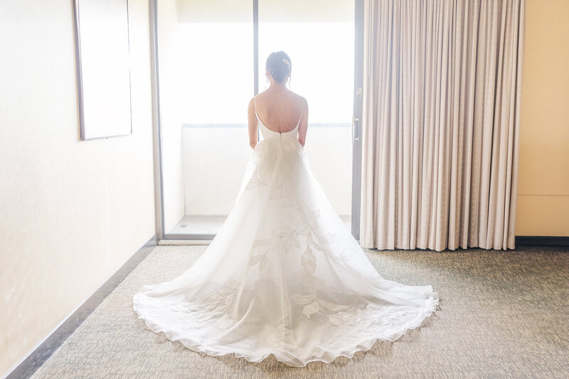 A bride shows off her dress while standing in a window to a Saginaw Wedding Photographer