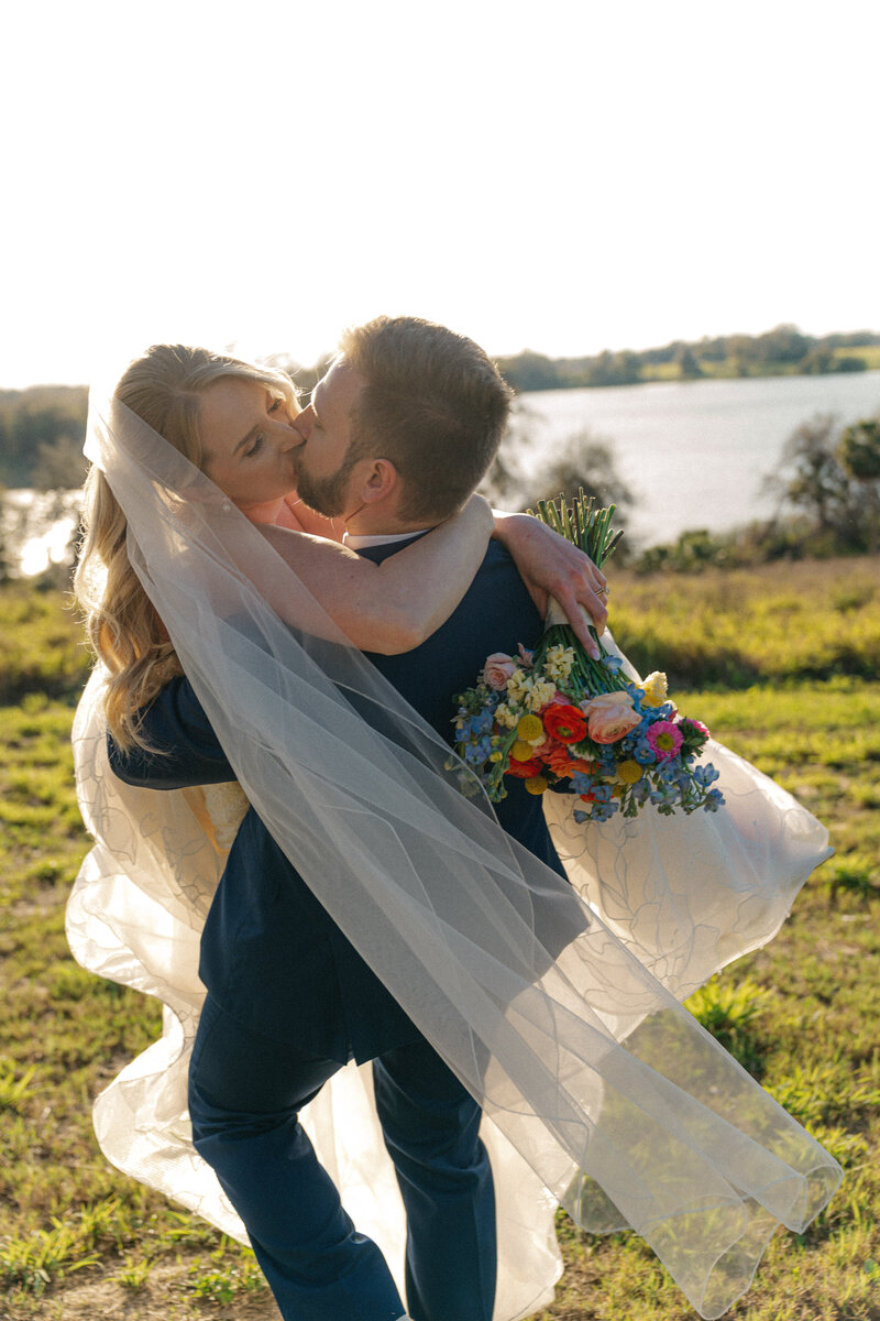 Bride and groom kissing in the field in front of lake at Lakeview Gardens