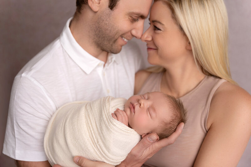 mom and dad holding and smiling at their newborn baby together in the nursery