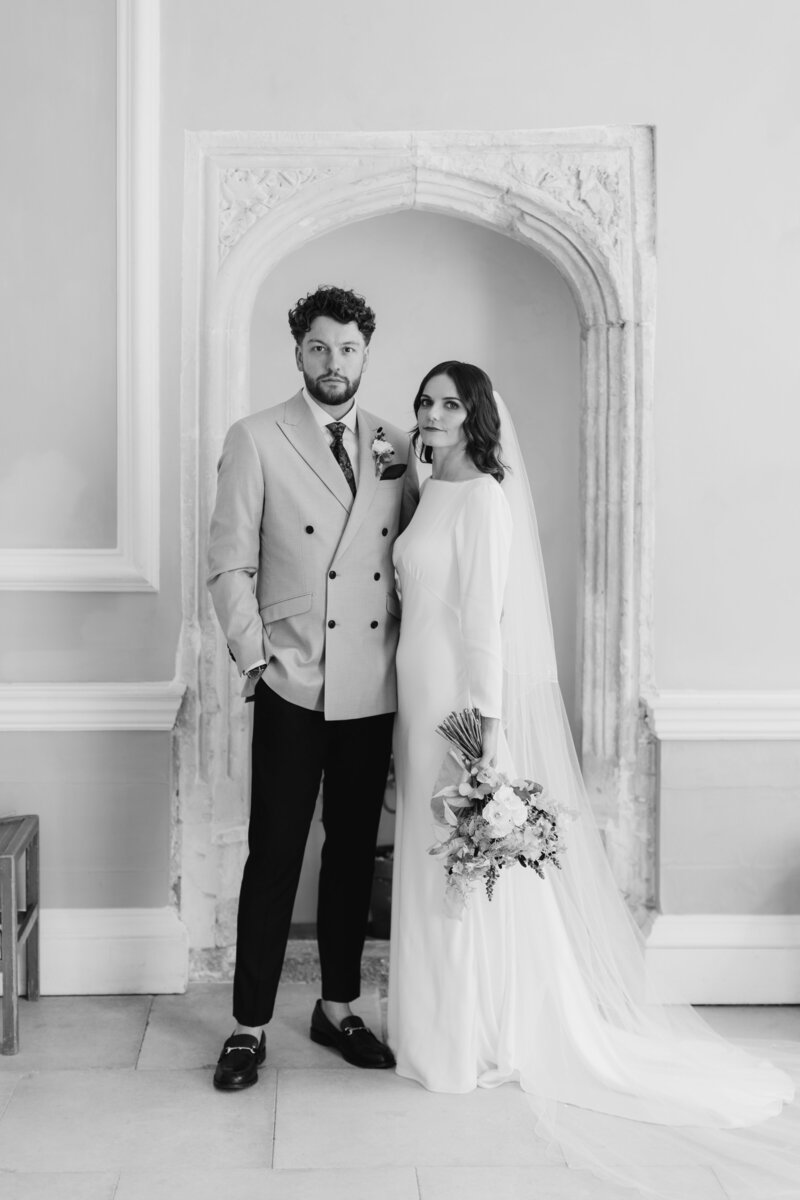 Black and white editorial style wedding photo of bride and groom portrait in front of old fireplace at historic british stately wedding venue