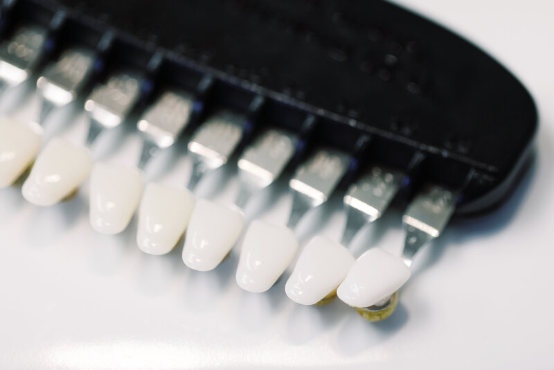 Shades of teeth samples arranged in a row, showcasing a gradient of colors from a natural white to a darker yellowish tone. Each sample is labeled with a number, representing different levels of whiteness, ranging from a bright, pearl-like white to a more off-white or slightly yellow shade. The samples are presented in a clear tray or holder, often used by dental professionals to assess the color of teeth for whitening treatments or cosmetic purposes.