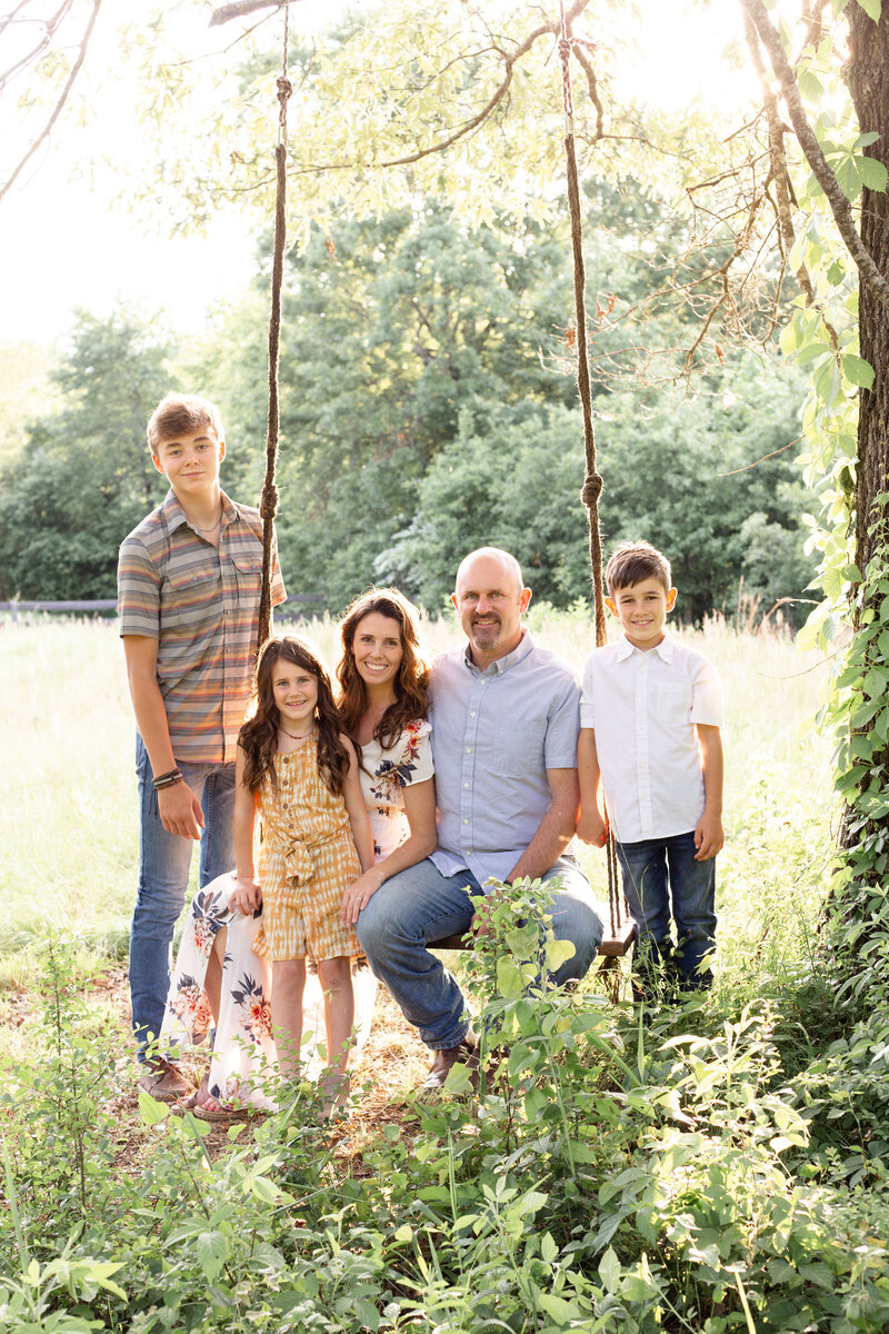 family sits on large swing in a feild