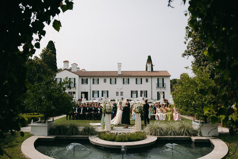 a wedding ceremony with a big white house in the background