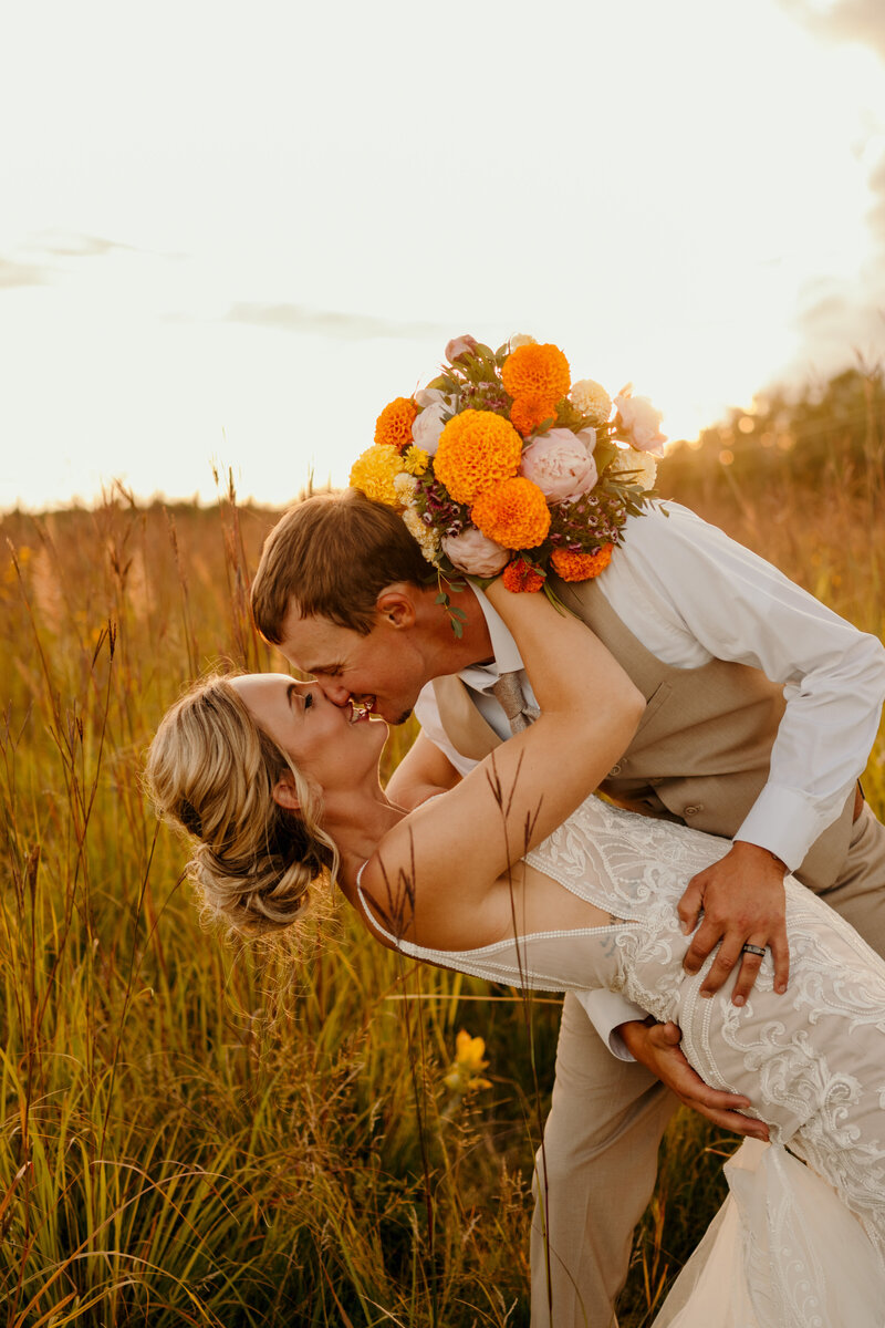 groom kissing bride in grass field