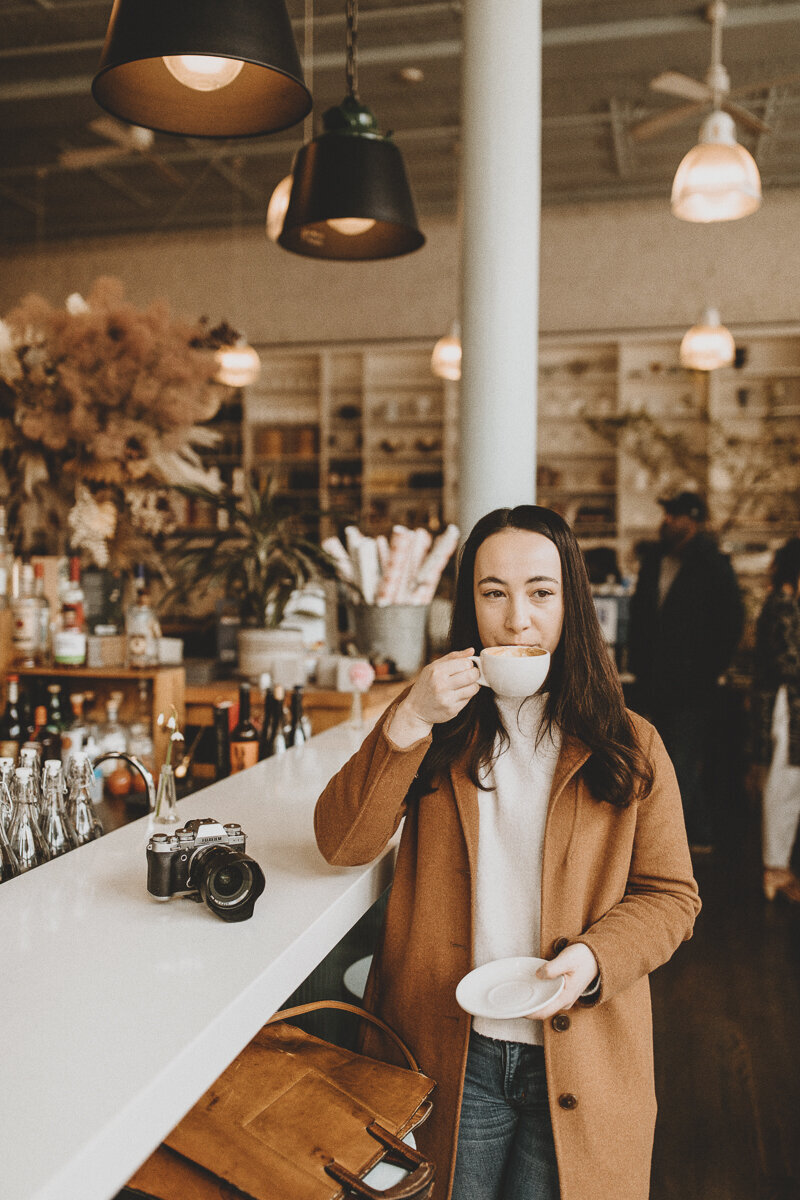 Seattle food photographer drinks coffee at coffee bar next to her camera