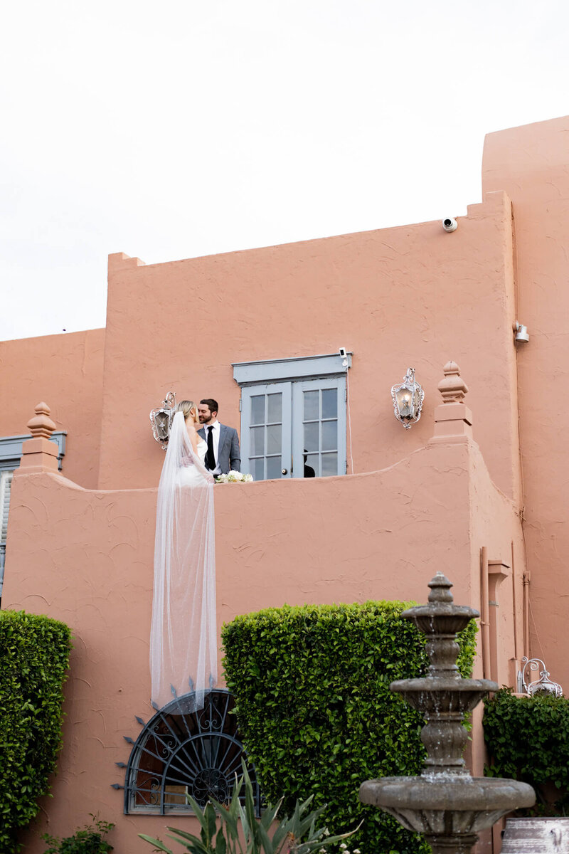 bride and groom on a balcony of a southwestern-style house, with her veil hanging over the balcony