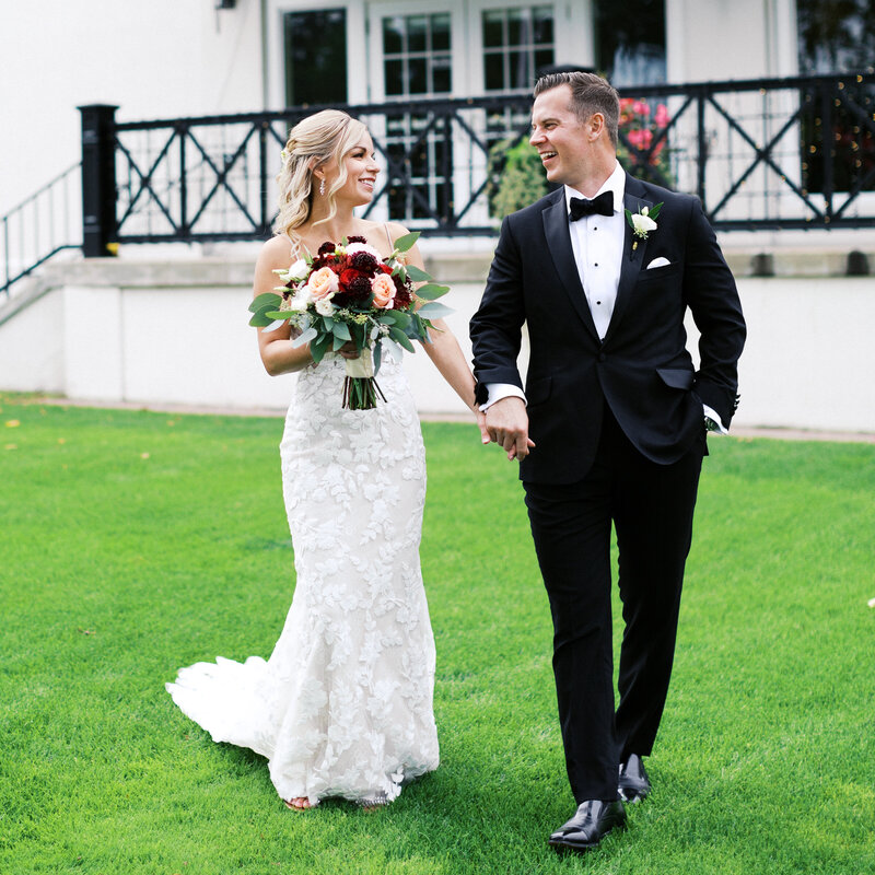 Newlyweds walking hand-in-hand at Minneapolis Golf Club, smiling lovingly at each other. A candid, romantic moment captured by Toly Dzyuba Photography, Minnesota wedding photographer.