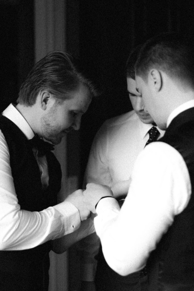 Groomsmen are helping the groom to put on the cufflinks in an image captured by wedding photographer Hannika Gabrielsson.