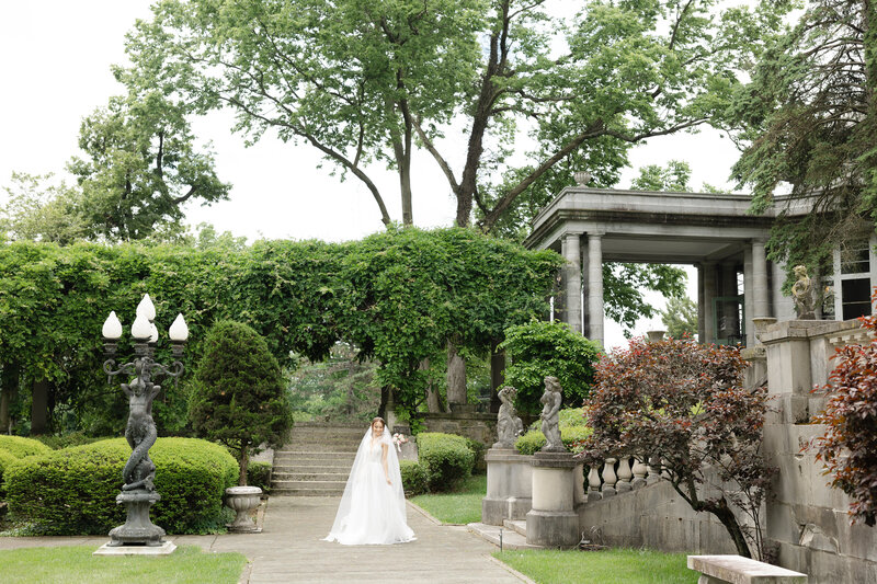 pulled back image of bride standing in garden outside of wedding venue
