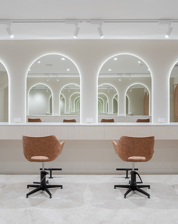 Minimalist salon design with dual tan chairs and glowing arched mirrors, emphasising luxury hair styling services for women.