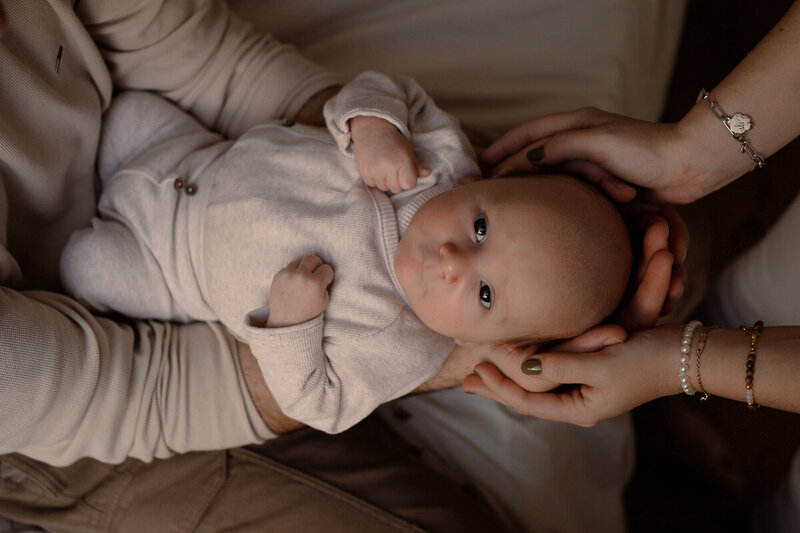 Baby wordt gedragen op papa's armen en moeder heeft handen rondom zijn hoofdje.
