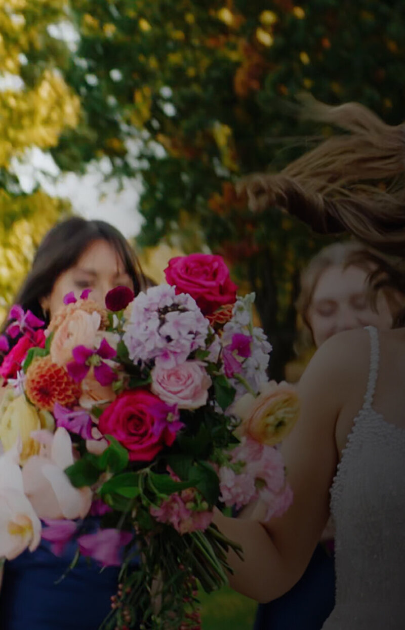 Snapshot from a Boston wedding film of the bride with her bridesmaid, surrounded by vibrant flowers