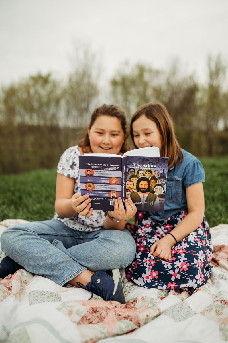 two girls sitting in yard on blanket reading a book together
