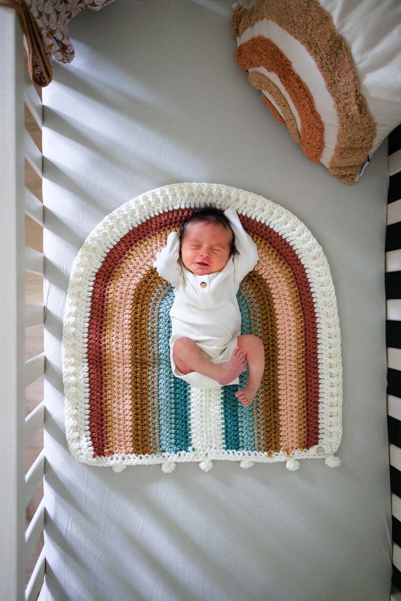 Overhead crib shot of newborn baby stretching.