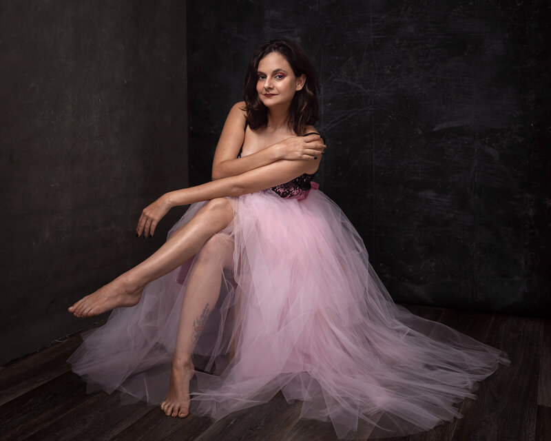 woman in long baby pink flowing dress seated in studio with legs crossed elegantly