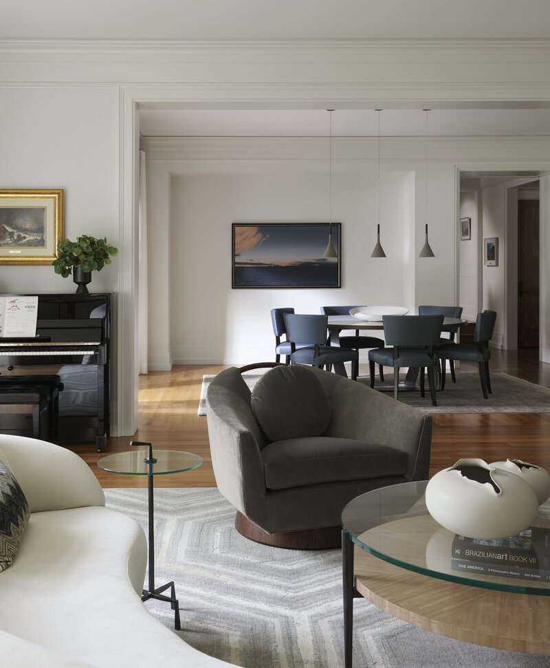Living room design, the room has light sage green walls, a grey sofa and matching chair, ornage pillows, a wooden baby brand piano, and white trimmed and marble fireplace on the wall centre