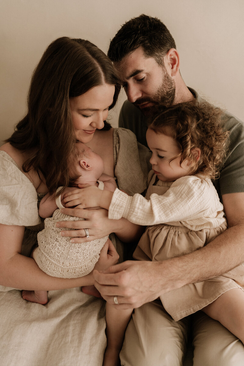 Newborn photography of big sister and baby brother on beanbag. Baby brother laying on his belly while his sister cuddles around his face and back. Eyes closed embracing her cuddle