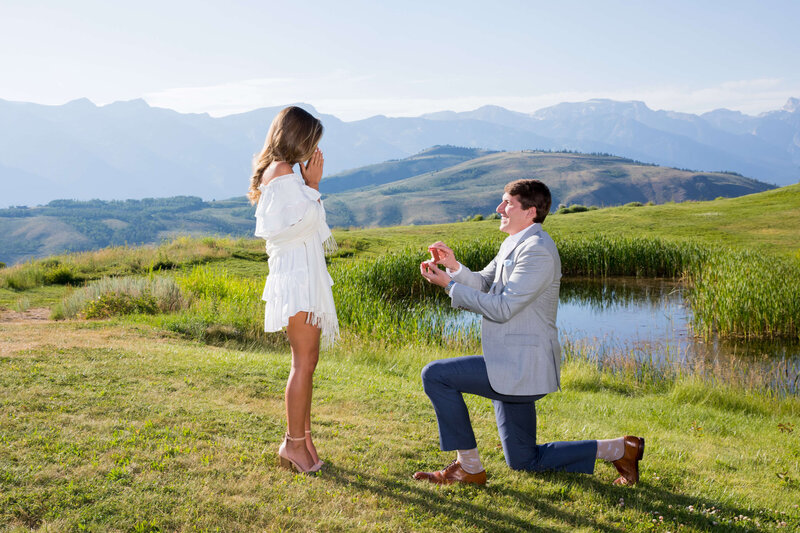 Romantic proposal at Amangani, as a groom-to-be kneels with a ring, surrounded by rolling hills and a peaceful pond in Jackson Hole.