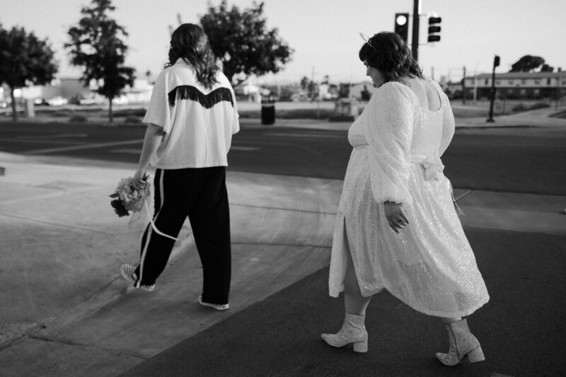Black and white photo of a wedding couple walking across a street.