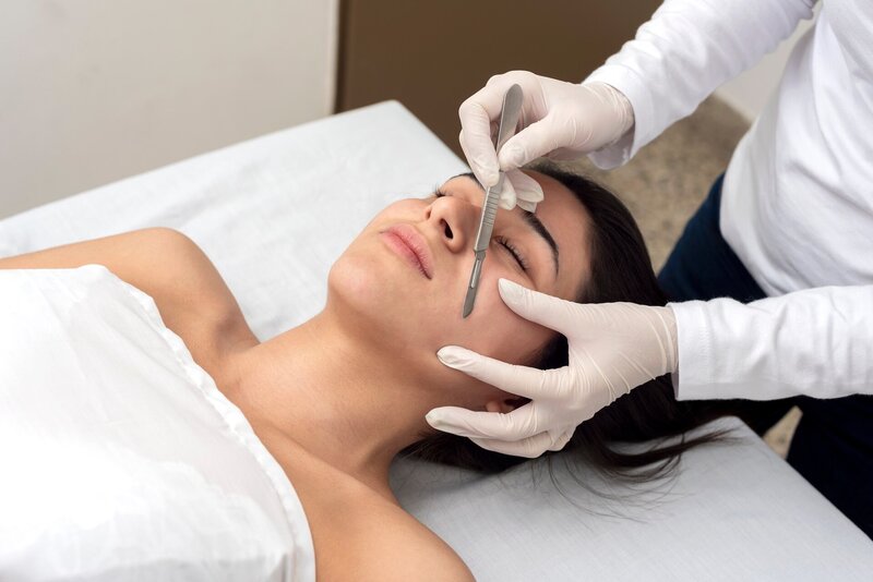 Closeup image of a woman lying down getting a dermaplaning facial treatment from an esthetician wearing white gloves