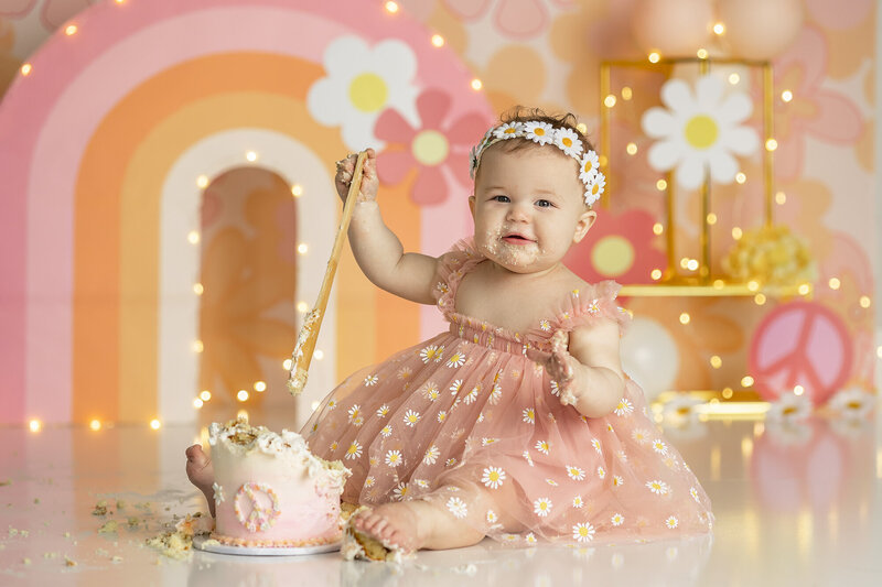 1 year old having fun in a cake smash session sitting on yellow backdrop
