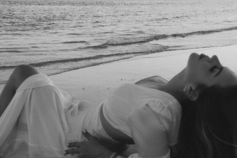 a Bride sitting on a beach during her braidal portraits as the waves crash and the sun sets behind her in Miami, FL, created by Andrea-Marie Photography