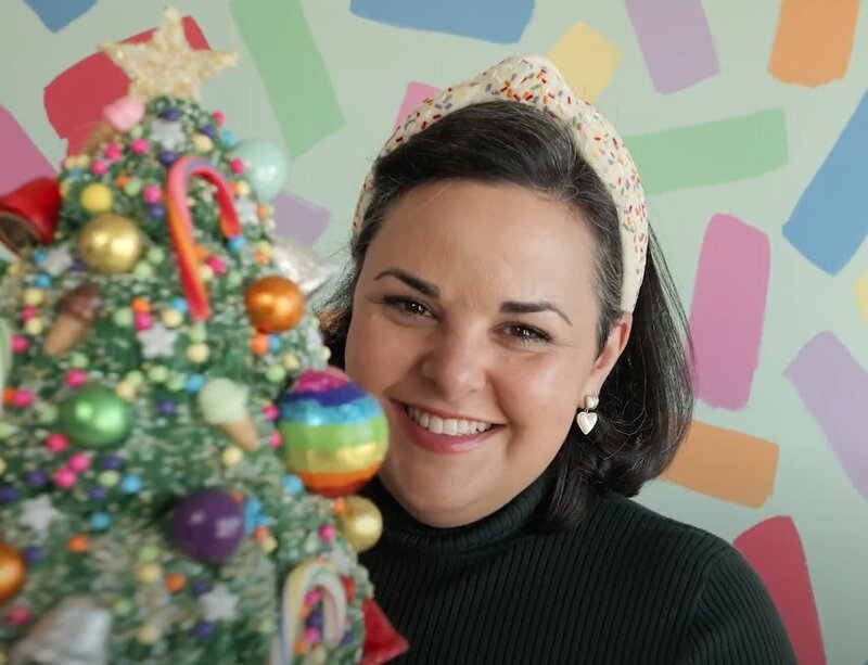 A person smiling in front of a christmas tree cake 