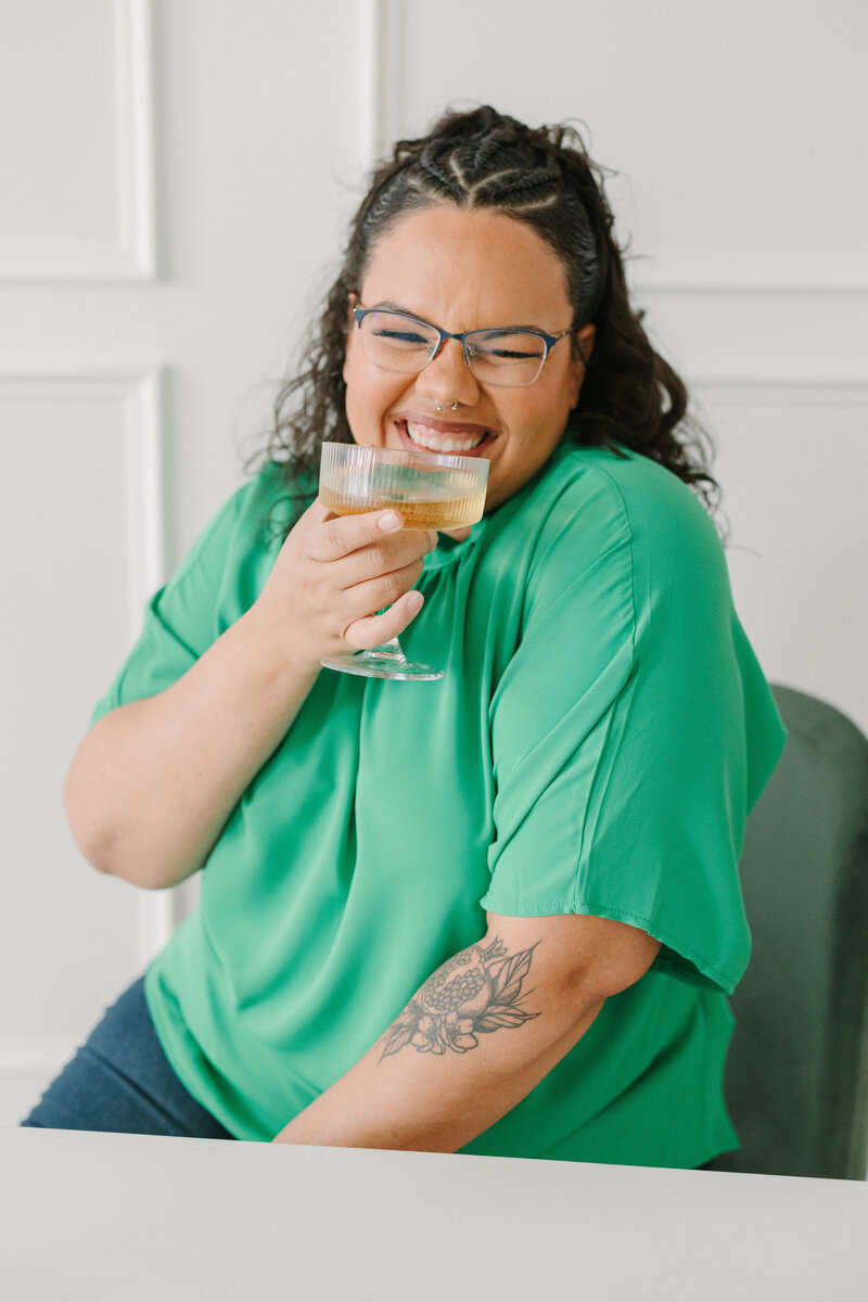 A person smiling big with a cocktail glass up to their lips