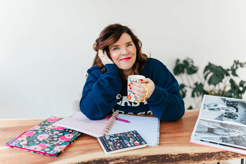 woman with dark hear and bright pink lipstick holding mug and smiling for camera