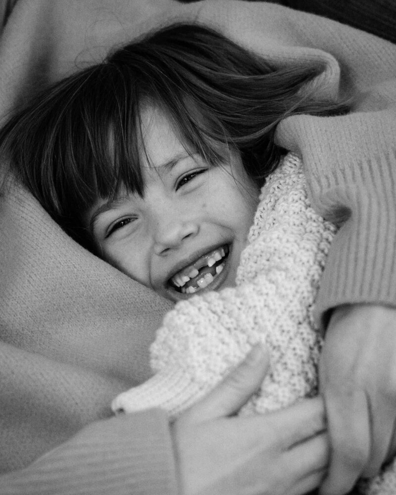 Joyful child mid-laugh, missing front teeth and snuggled close in warm embrace during a relaxed Munich family photo session