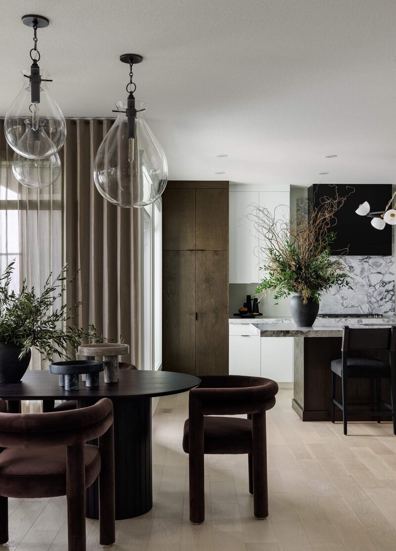 A dining room and kitchen space with dark velvet dining chairs and brown cabinets. 