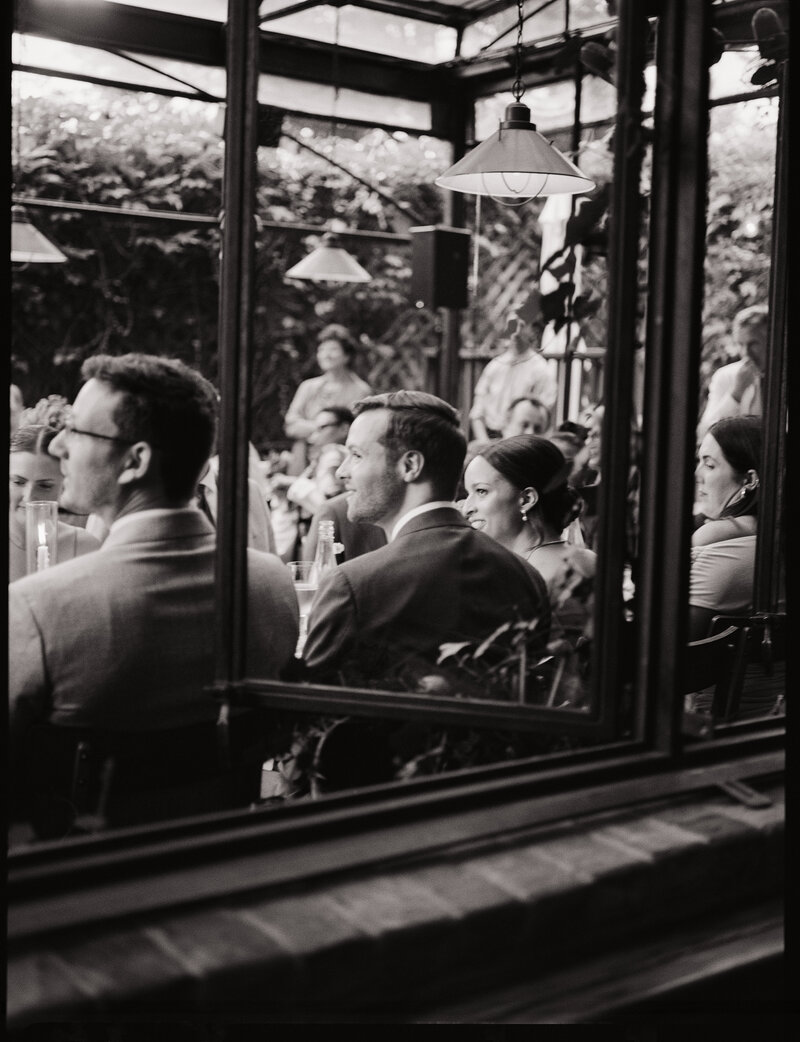 Black-and-white documentary wedding photography of guests gathered for an intimate Brooklyn wedding reception in a cozy garden setting