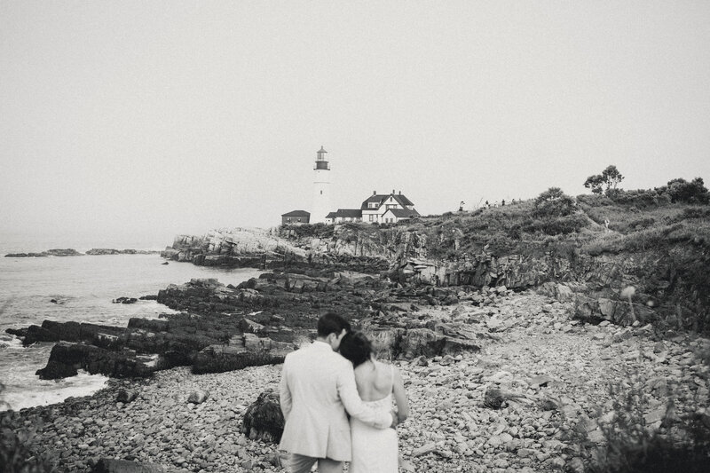 Bride and groom walking hand in hand along the rocky coastline during their Maine wedding.
