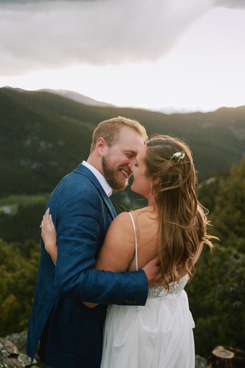 A bride and groom on a mountain overlook about to kiss.