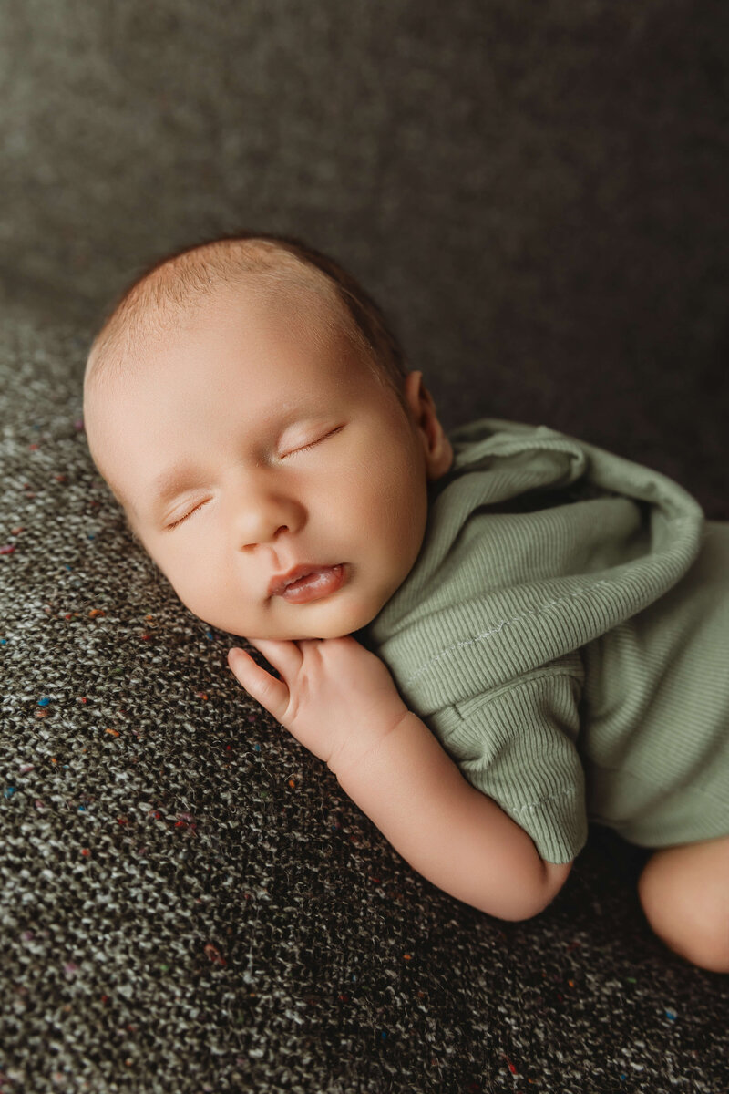 baby boy sleeping with his hands under his head in a green onesie on a green plant background newborn harrisburg photos